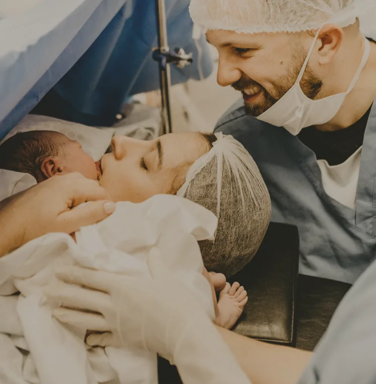Mother and newborn together moments after birth, with a smiling birth partner nearby